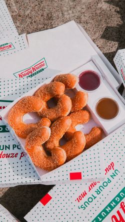 Box of sugar-coated doughnuts with two dipping sauces from Krispy Kreme - CC Qwartz displayed on a speckled surface.