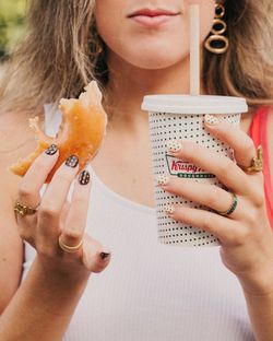 Personne tenant un doughnut partiellement mangé et un gobelet de café Krispy Kreme à emporter.
