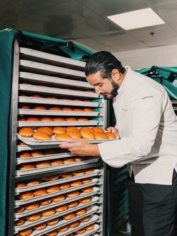 Un employé retire une plaque de pâtisseries dorées prêtes à être servies dans une cuisine professionnelle.