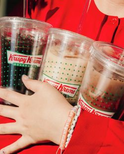 Trois boissons glacées Krispy Kreme en gobelets transparents tenues par une main avec un bracelet perlé.