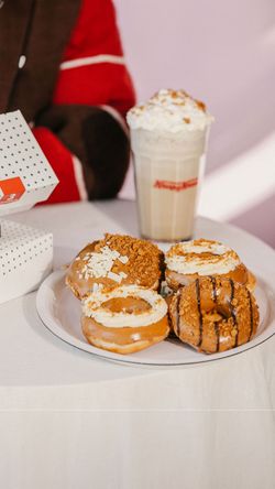 Four assorted Krispy Kreme doughnuts on a plate with a tall iced coffee drink in the background.