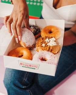 A box of assorted Krispy Kreme doughnuts held by a person, featuring glazed, powdered, and topped varieties.