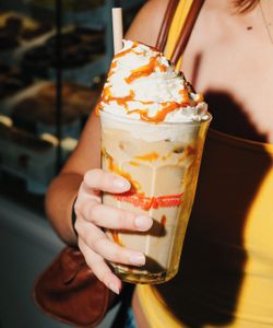 Café glacé avec chantilly et caramel dans un gobelet Krispy Kreme tenu par une personne en top jaune.