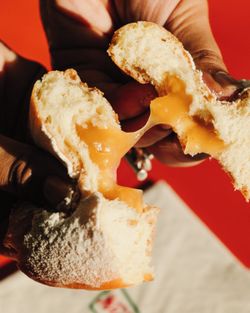 Un doughnut fourré de crème fondante et légèrement poudré, tenu et ouvert à la main sur fond rouge.