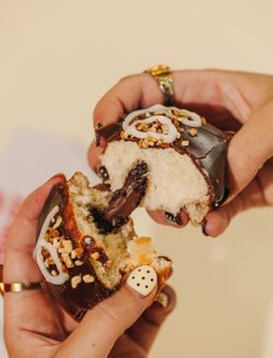 Beignet au chocolat garni d'un coeur fondant, décoré de noix et de glaçage blanc, tenu par deux mains.