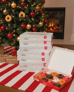 Boîtes de doughnuts Krispy Kreme près d'un sapin de Noël, avec des pâtisseries festives en premier plan.