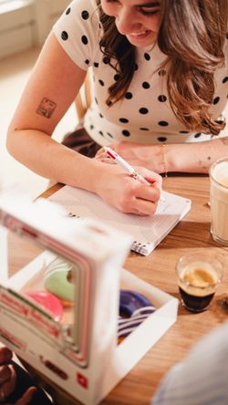 Personne écrivant dans un carnet avec café et boîte de doughnuts de Krispy Kreme sur la table.