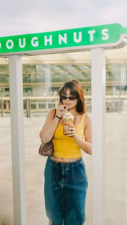 Une femme boit un café à emporter devant un stand de doughnuts au Krispy Kreme - CC Beaugrenelle.