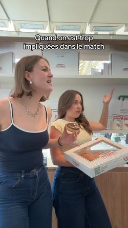 Two women inside Krispy Kreme store holding doughnuts, with Krispy Kreme doughnut boxes visible in the background.