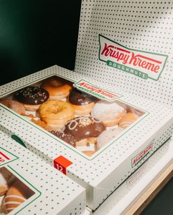 Box of assorted Krispy Kreme doughnuts with multiple flavors, in branded white green polka dot packaging.
