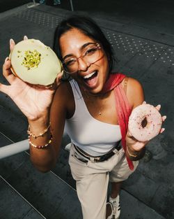 Person holding two doughnuts topped with pistachios and pink icing in an outdoor urban setting.