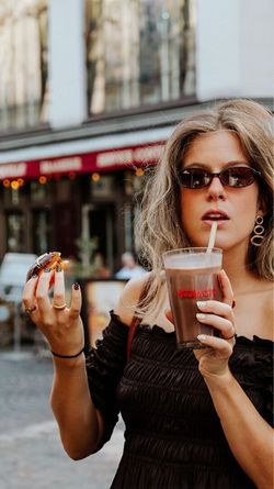 Femme tenant un doughnut et un café à emporter devant Krispy Kreme - CC Qwartz pour un petit-déjeuner ou dessert.