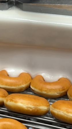 Doughnuts chauds en train d'être glacés sur une grille, préparés à Krispy Kreme.