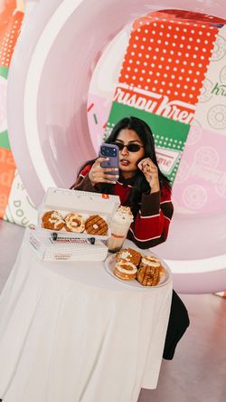 Doughnuts variés et boissons sur une table avec une personne prenant une photo chez Krispy Kreme - CC Beaugrenelle.