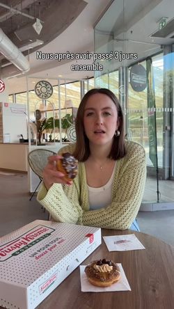A person holding a decorated doughnut inside Krispy Kreme with a doughnut box and another doughnut on the table.