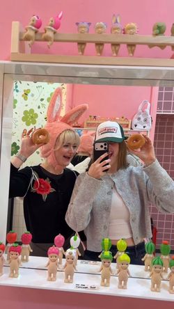 Deux femmes souriantes portent des beignets Krispy Kreme, avec un décor coloré en arrière-plan.
