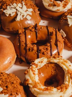 Doughnuts glacés au chocolat avec crèmes et éclats croquants, parfaits pour dessert ou café à emporter chez Krispy Kreme.