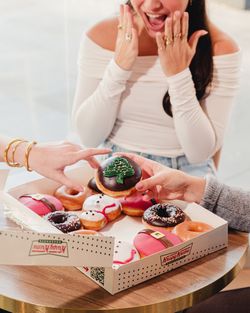 Une boîte de beignets variés de Krispy Kreme, avec des décorations festives, sur une table.