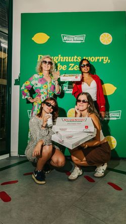 Quatre femmes portant des lunettes de soleil tiennent des boîtes de doughnuts Krispy Kreme devant un fond vert citron.