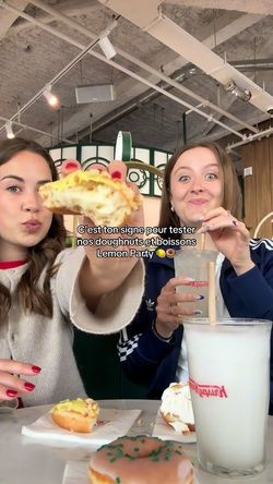 Two people enjoying doughnuts and drinks inside Krispy Kreme, showcasing desserts and café items.