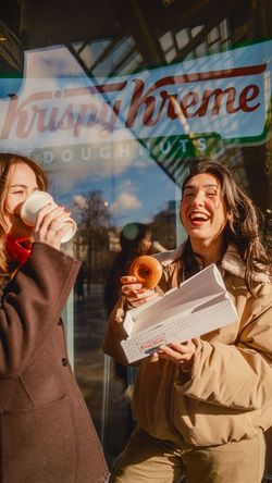 Deux femmes dégustant des doughnuts et café à emporter devant Krispy Kreme avenue de Clichy à Paris