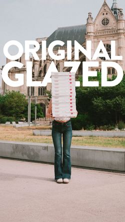 Person holding a tall stack of Krispy Kreme doughnut boxes outdoors near historic architecture.