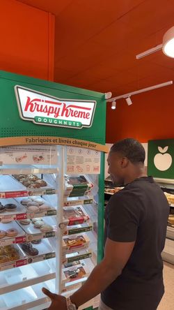 Présentoir lumineux de doughnuts Krispy Kreme avec un client faisant son choix à Paris avenue de Clichy.