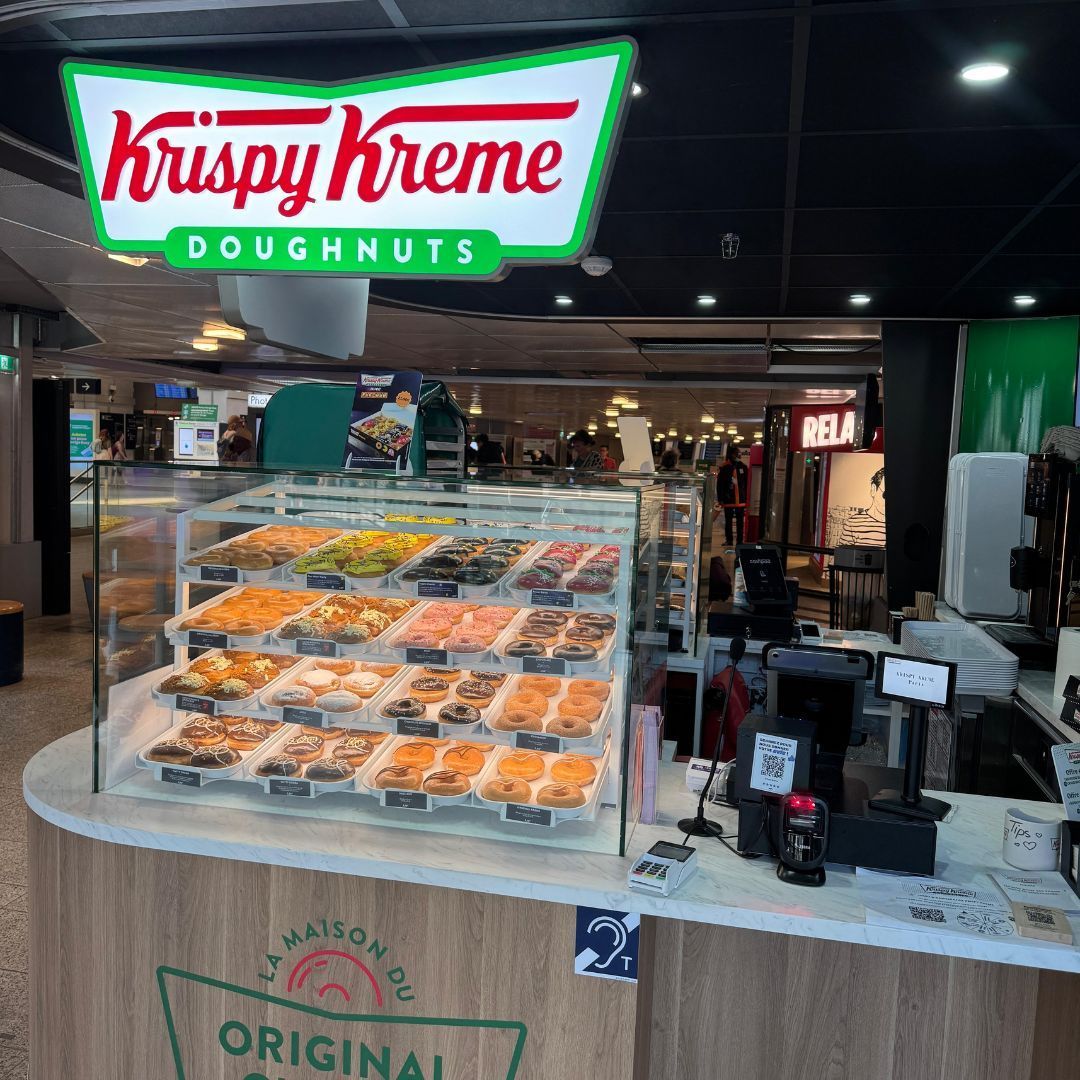 Vitrine de beignets variés au café Krispy Kreme à Gare de Montparnasse, offrant desserts et petit-déjeuner.
