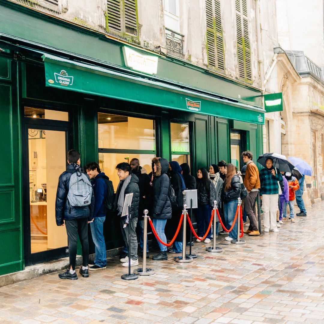 Nombreux clients faisant la queue devant le café Krispy Kreme à Paris, spécialisé dans les donuts et pâtisseries.