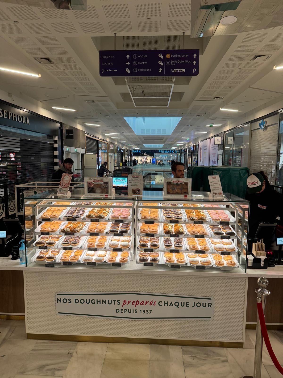 Doughnuts variés disponibles dans une pâtisserie moderne avec café à emporter.