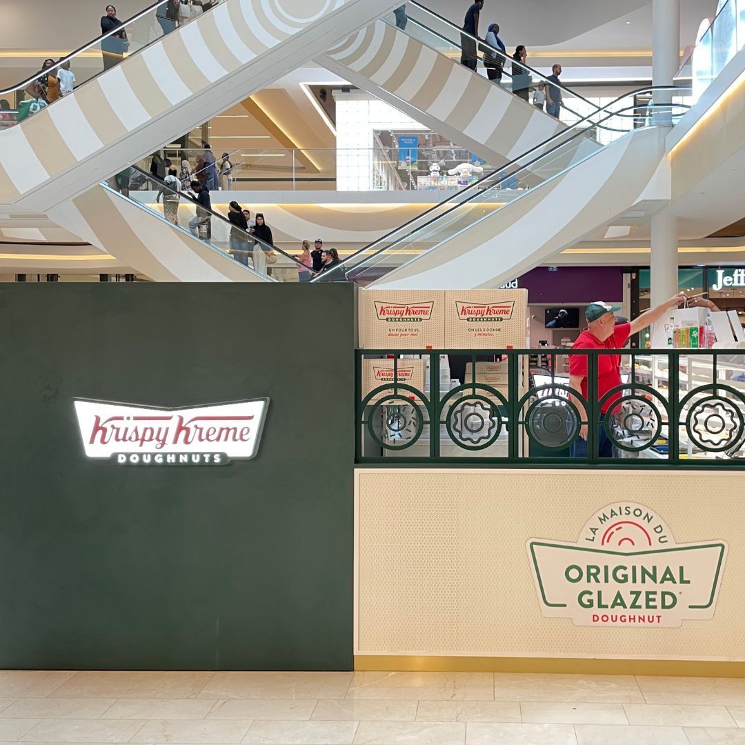 Krispy Kreme shop featuring a prominent sign and display of Original Glazed doughnuts in a shopping center.