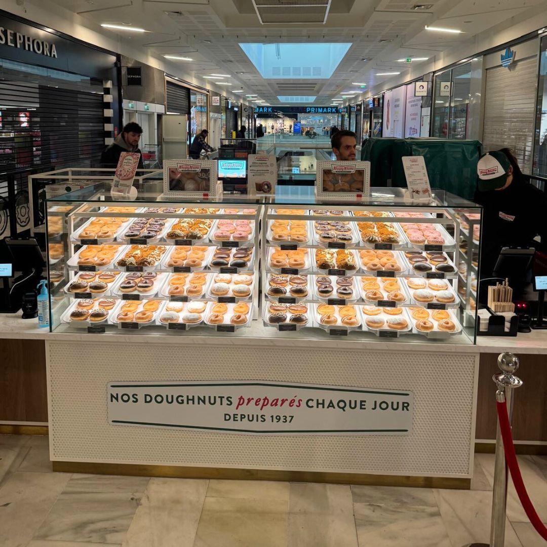 Stand présentant des doughnuts colorés, pâtisserie et café à emporter, ouvert pour le petit-déjeuner.