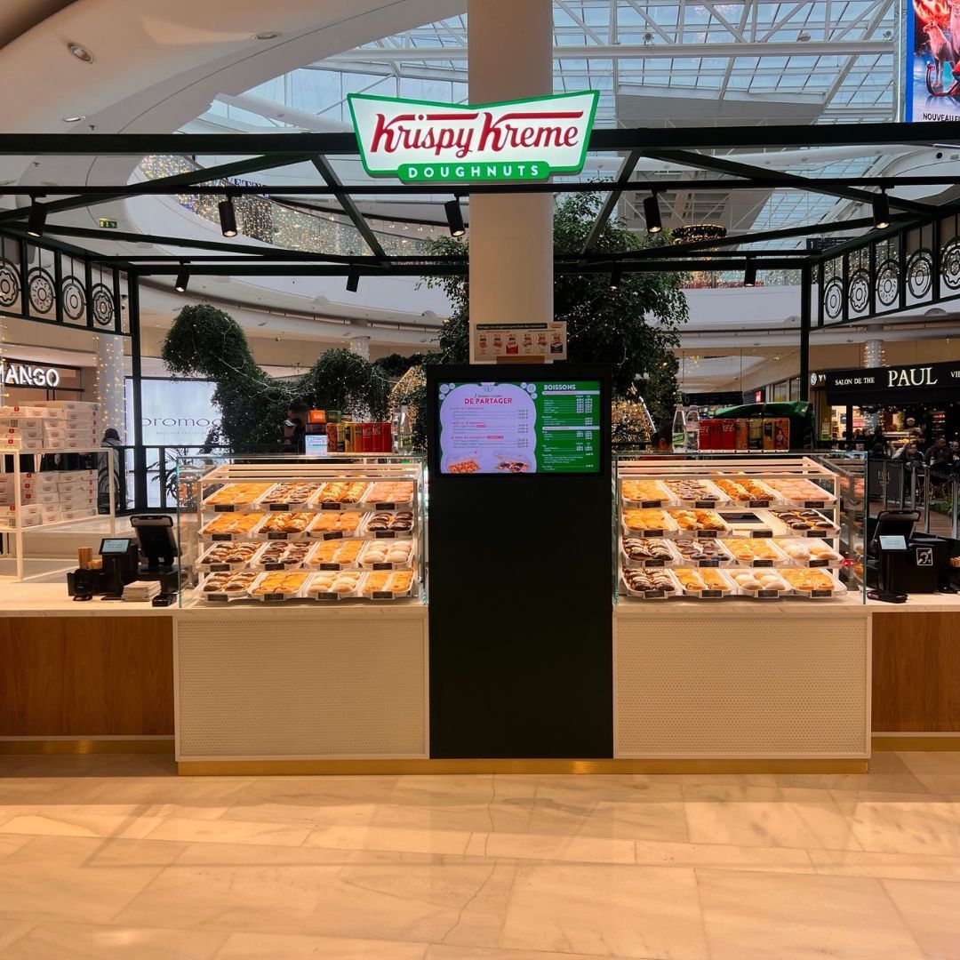 Vitrine de Krispy Kreme présentant une sélection de doughnuts, café à emporter et pâtisseries.