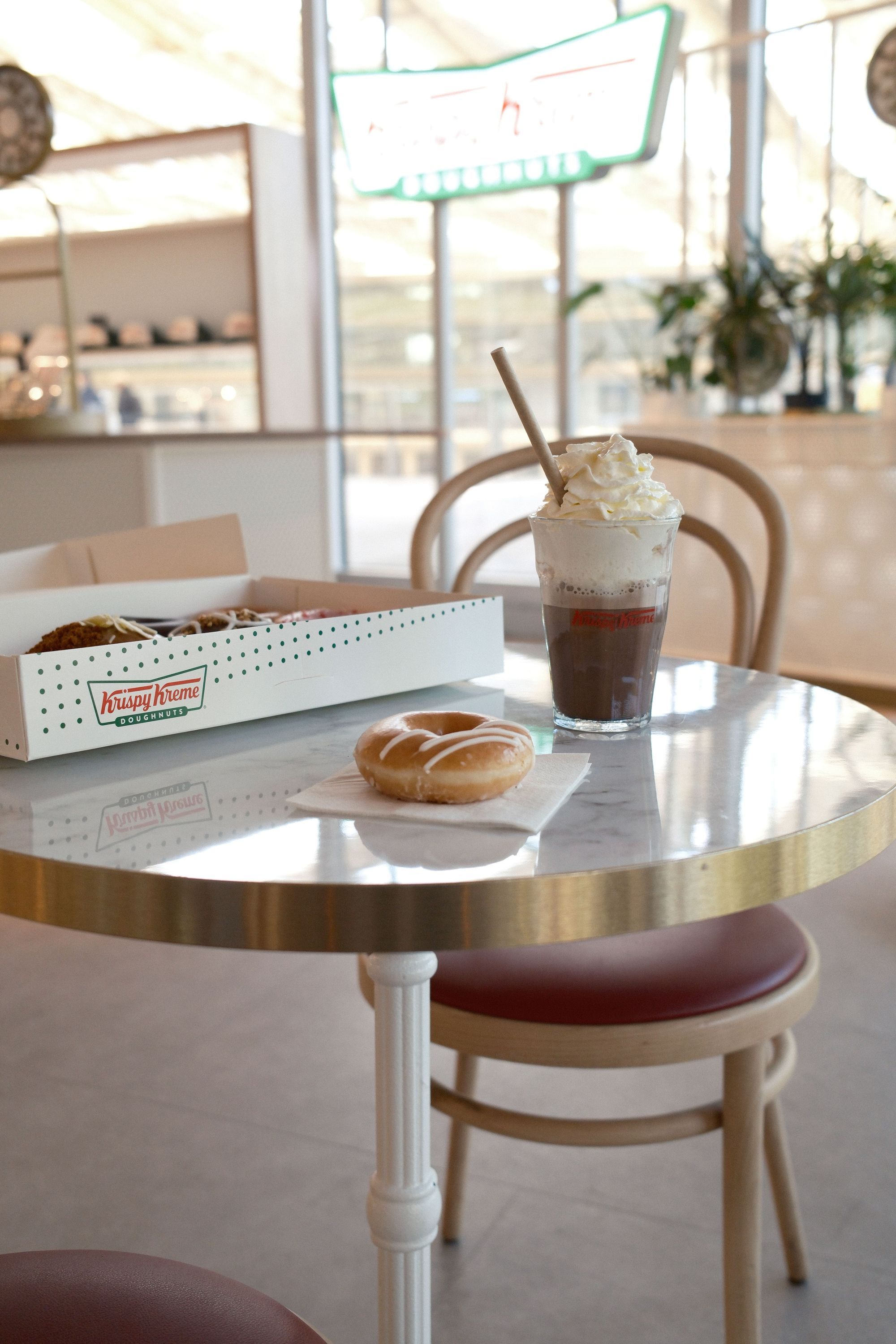 Un café avec un dessert à base de doughnut et un café à emporter sur une table, en arrière-plan un logo Krispy Kreme.