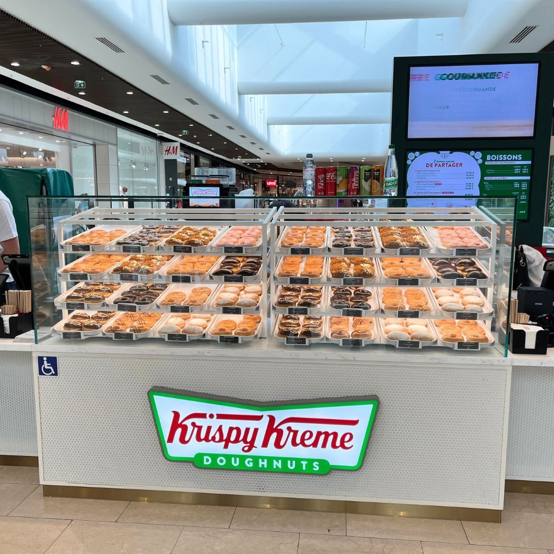 Vitrine de Krispy Kreme avec une sélection de donuts variés, idéal pour le petit-déjeuner ou en dessert.
