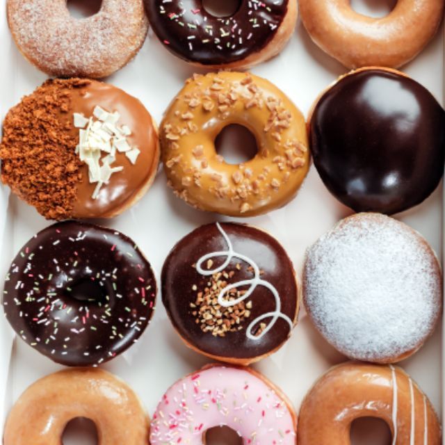 Doughnuts variés avec différentes garnitures et glaçages, présentés en rangées dans une boîte.