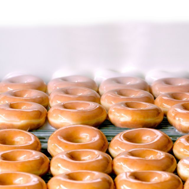 Doughnuts glacés alignés en rangées, montrant leur texture brillante et appétissante, typiques chez Krispy Kreme.