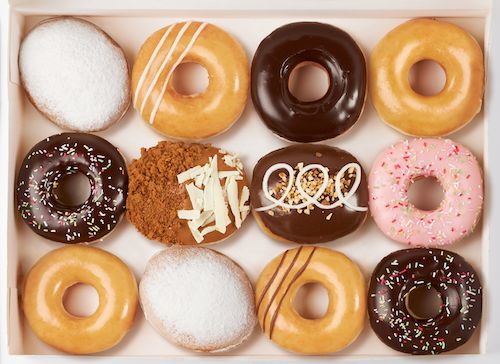 Assorted Krispy Kreme doughnuts with various glazes and toppings in a box for café takeaway.